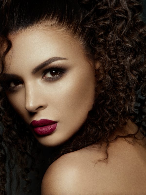 Beautiful face of a fashion model with black eyes.Curly hair. Pink lips. Studio portrait.